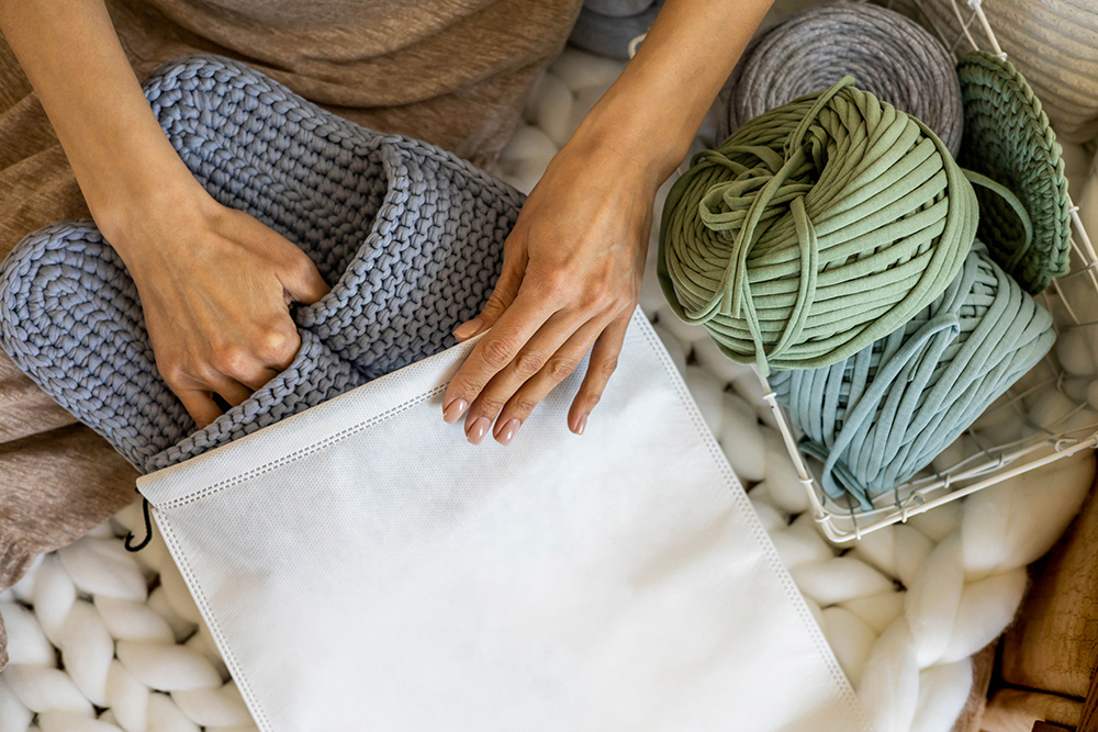 Woman preparing handmade slippers with thick yarn balls for knitting or crochet.