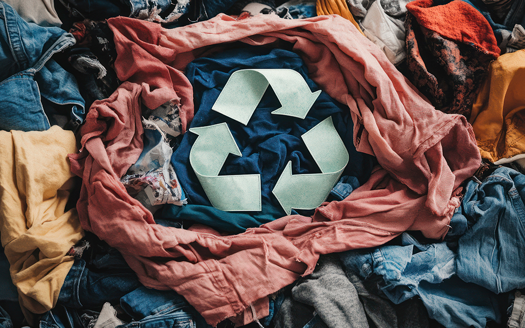 Recycling symbol surrounded by piles of discarded clothing, representing textile recycling and sustainable fashion.